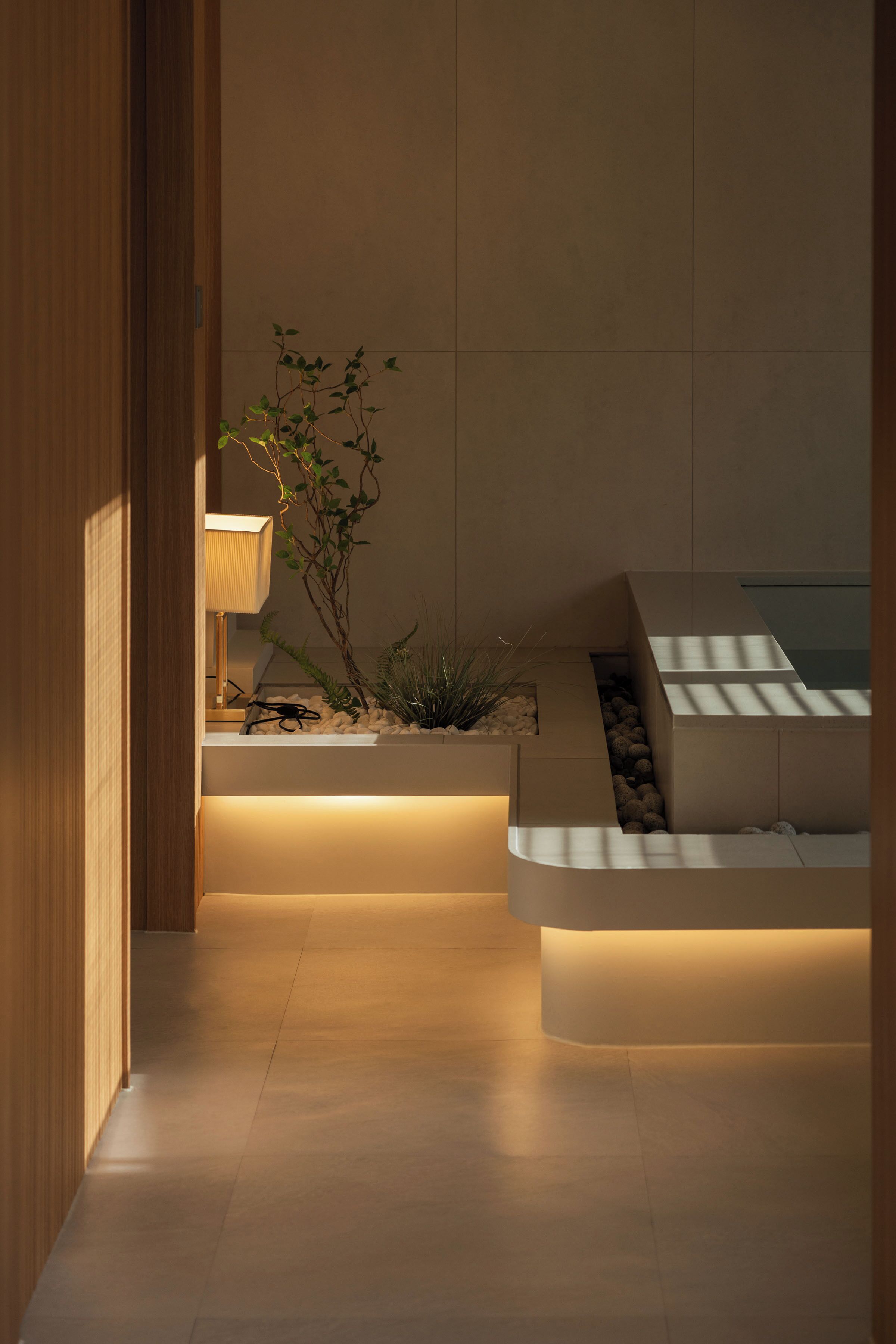 Ein modernes Interieur mit Holztür, beleuchteter Lampe, Pflanze und integriertem Sitzplatz.