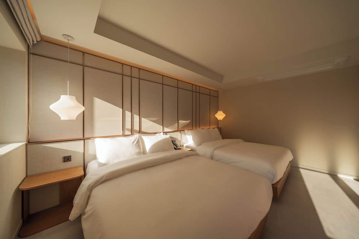 A modern bedroom with two beds, a wooden headboard, and a built-in shelf.