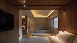 A modern bedroom with a large bed, a built-in TV, a walk-in closet, and a small bathroom with a bathtub. - ONSHIMJAE (Pocheon)