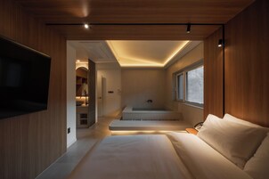 A modern bedroom with a large bed, a built-in TV, a walk-in closet, and a small bathroom with a bathtub.