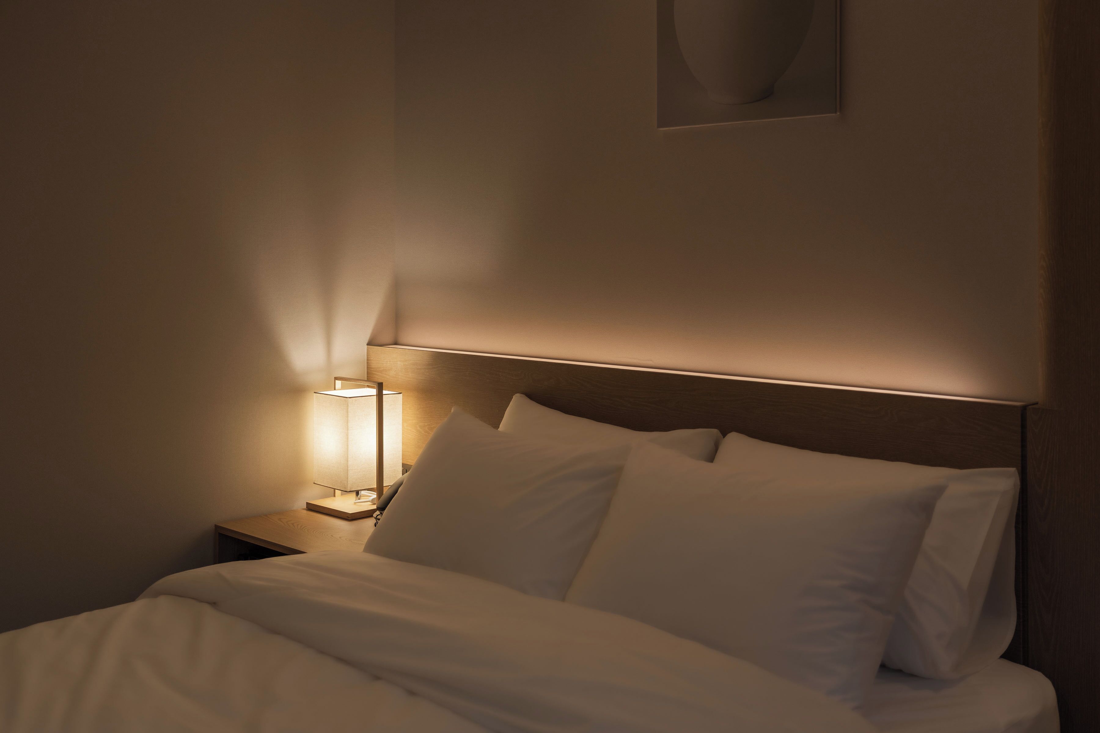 A neatly made bed with white linens, a bedside lamp, and a wooden headboard.