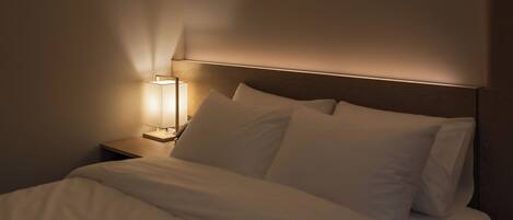 A neatly made bed with white linens, a bedside lamp, and a wooden headboard.
