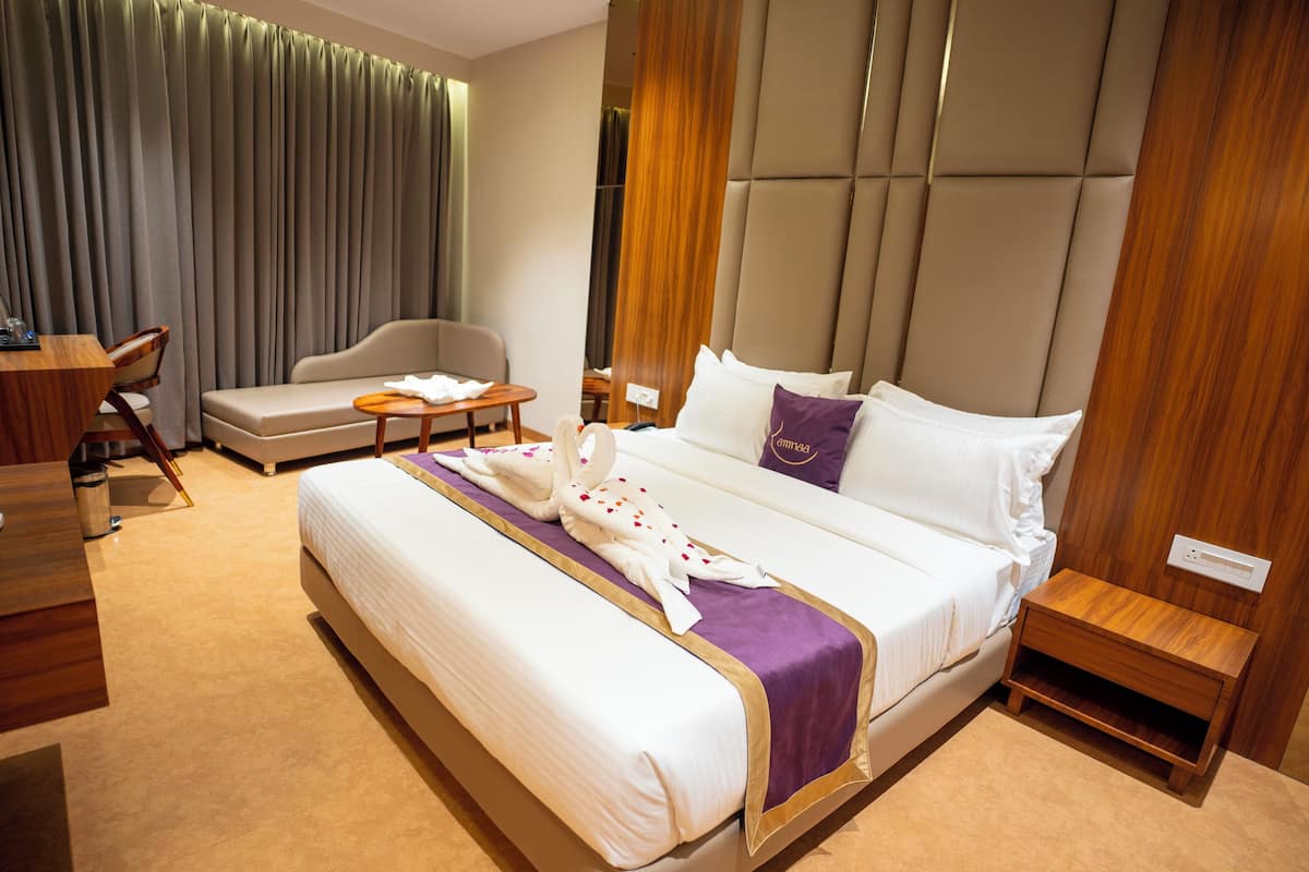 A hotel room with a large bed, a wooden nightstand, a desk with a chair, and a sofa.