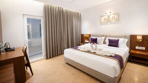 Een hotelkamer met een groot bed, een bureau met stoel, een balkon met gordijnen en een plafondventilator.