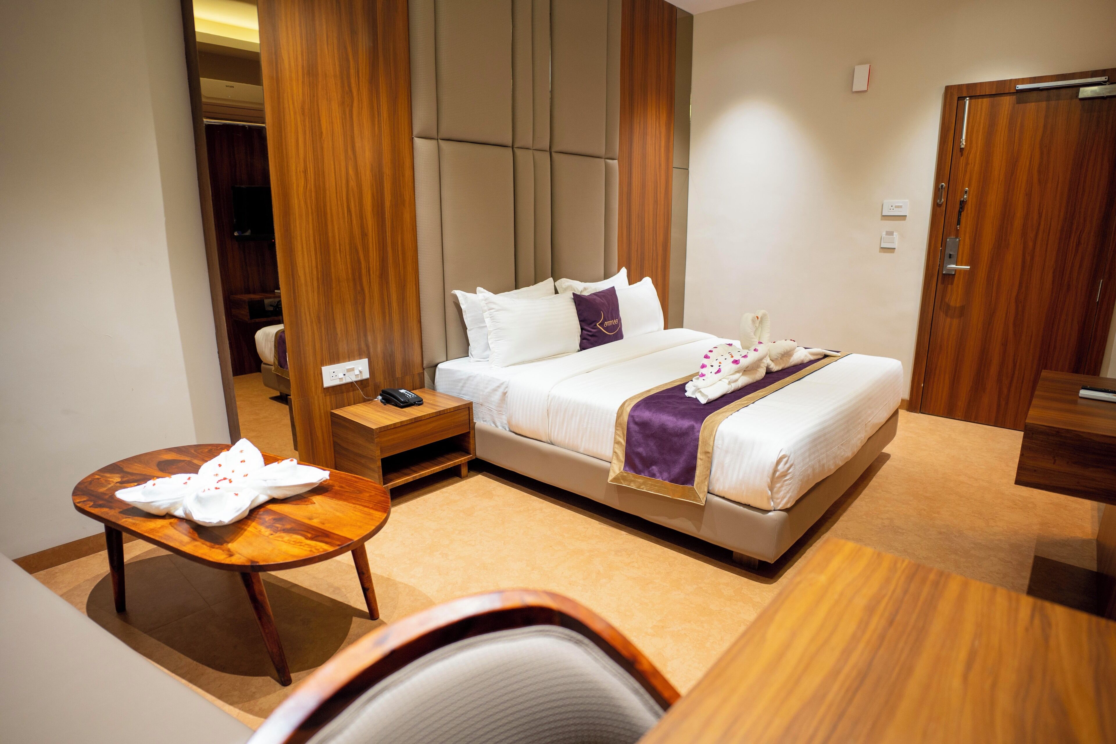 A hotel room with a bed, bedside table, chair, and a small table with a towel.