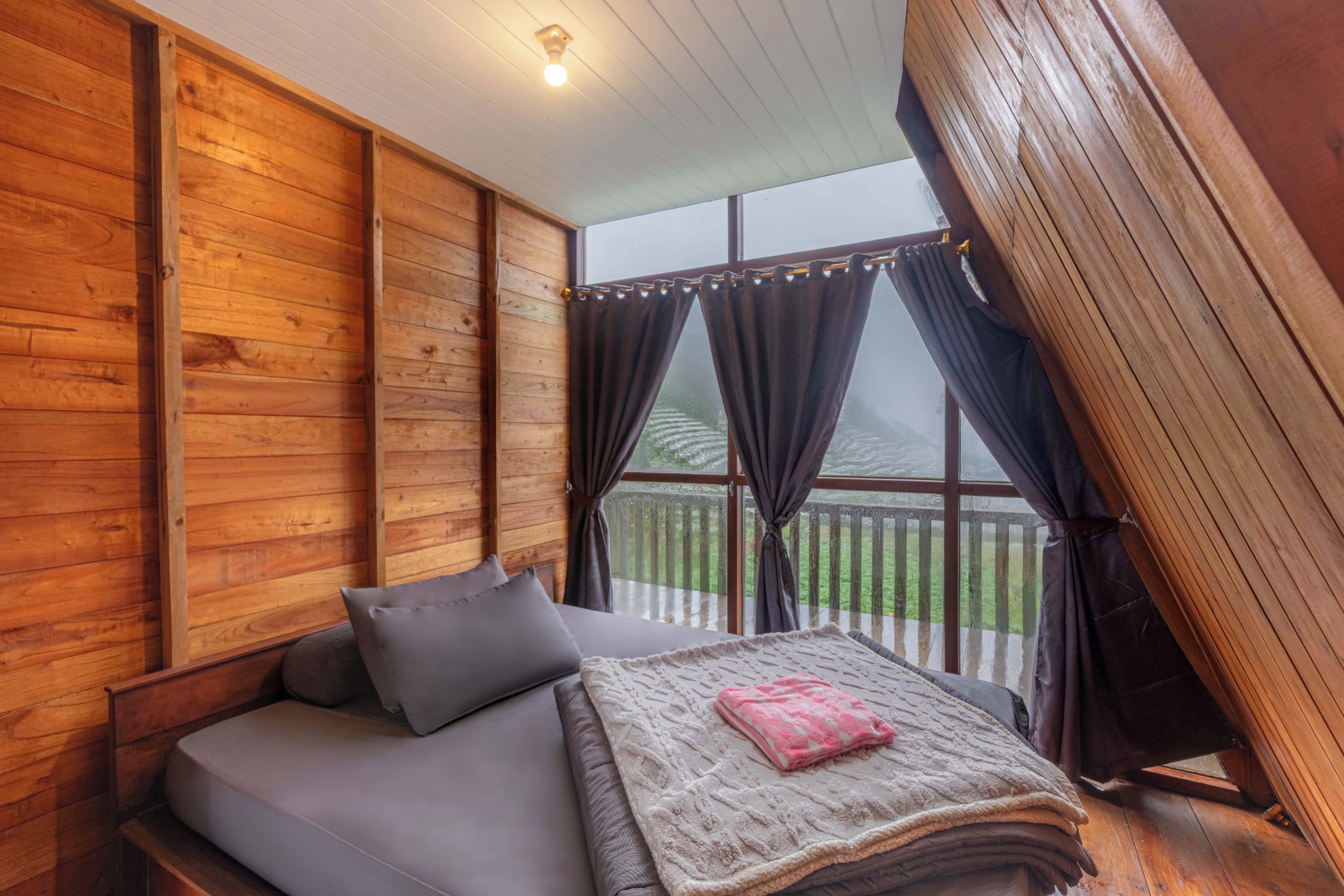 Una habitación acogedora con una cama, un ventanal con cortinas y techo de madera.
