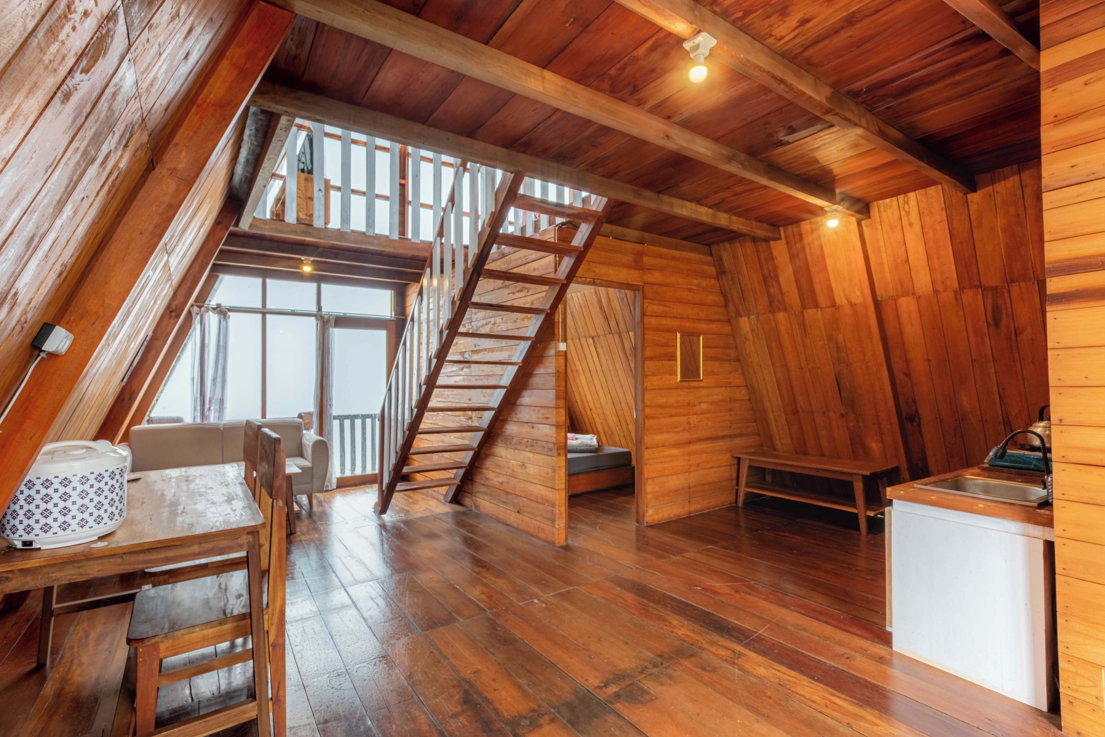 Interior em madeira com quarto em mezanino, área de jantar e cozinha compacta.