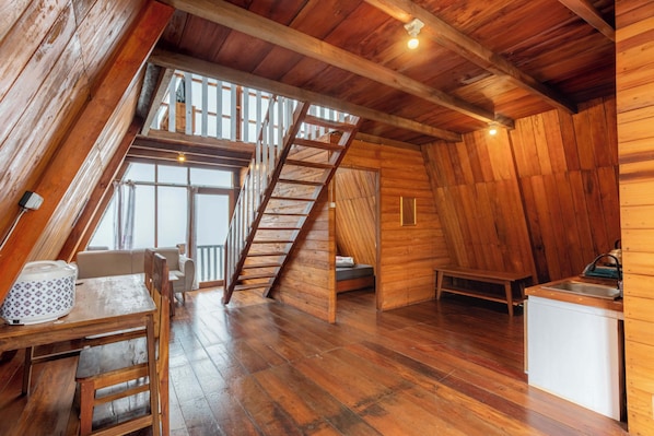A wooden interior with a loft bedroom, a dining area, and a kitchenette. - Padangsari Cabin 2 (Kejajar)
