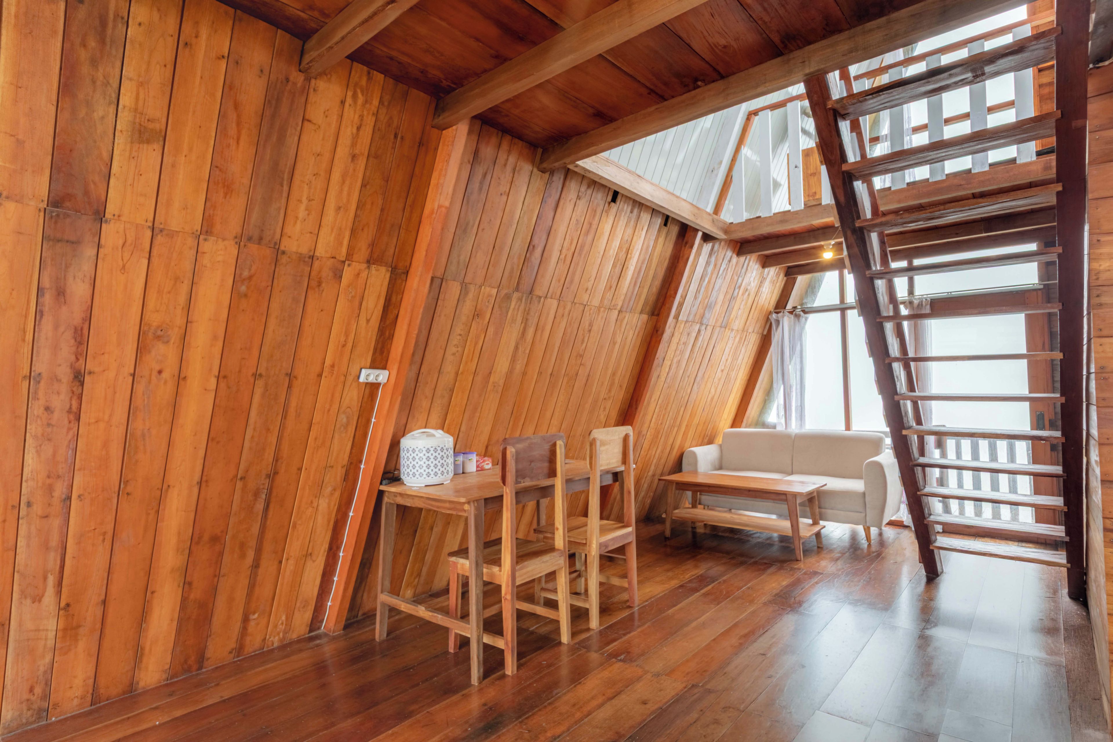Una habitación con paredes de madera inclinadas, una mesa de madera con sillas, un sofá y una escalera.