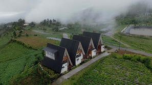A rural landscape with a row of houses with steep roofs, surrounded by terraced fields and a misty atmosphere. - Padangsari Cabin 2 (Kejajar)