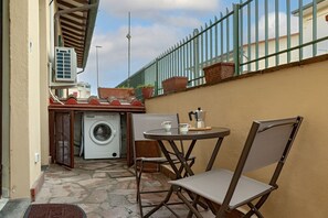 A small outdoor patio with a washing machine, a table with chairs, and a metal fence. - Homiday – Incanto is a bright and cozy apartment located on Via Pietrasantina, just a few minutes’ walk from the Leaning Tower of Pisa and Piazza dei Miracoli.Situated in a convenient and quiet area, it allows you to experience the city stress-free.  (Pisa)