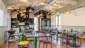 Interior de un restaurante con varias mesas, sillas, lámparas de mimbre colgantes y una zona de bar con estanterías.