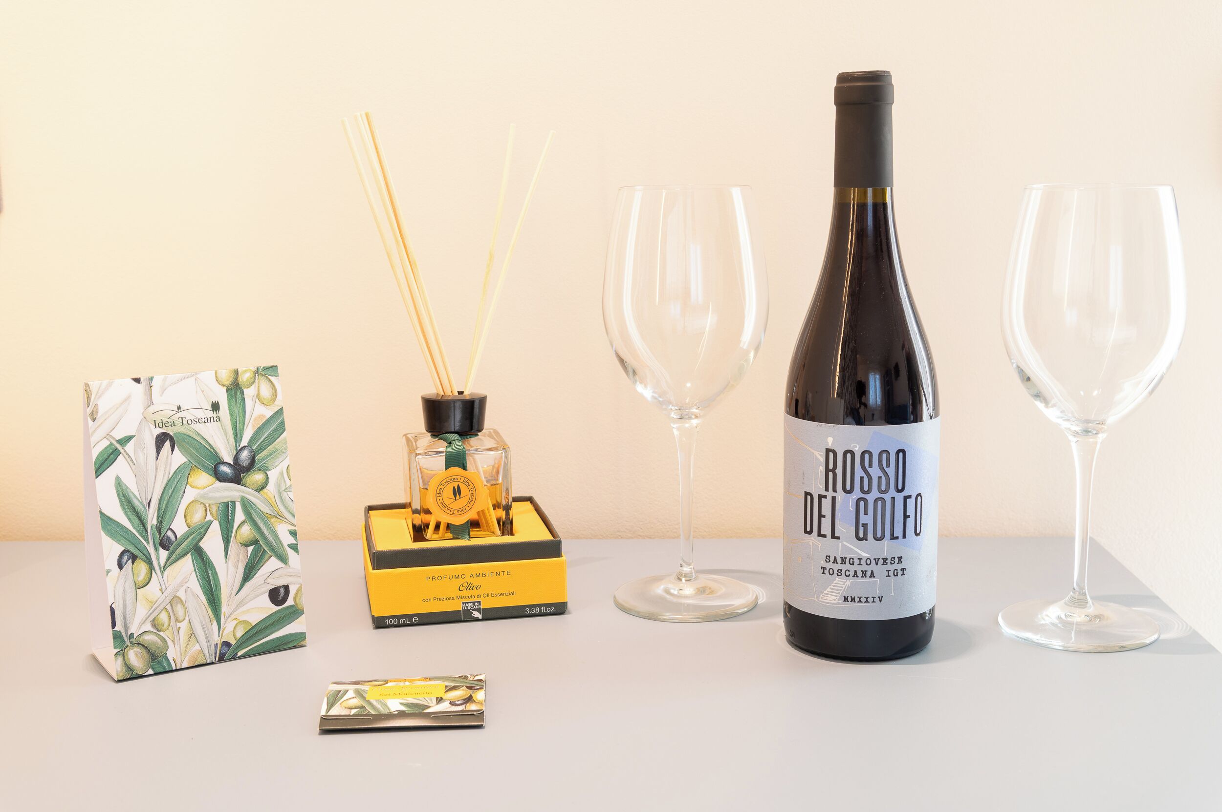 A bottle of Rosso del Golfo wine, two empty wine glasses, a box of incense sticks, and a scented candle on a table.
