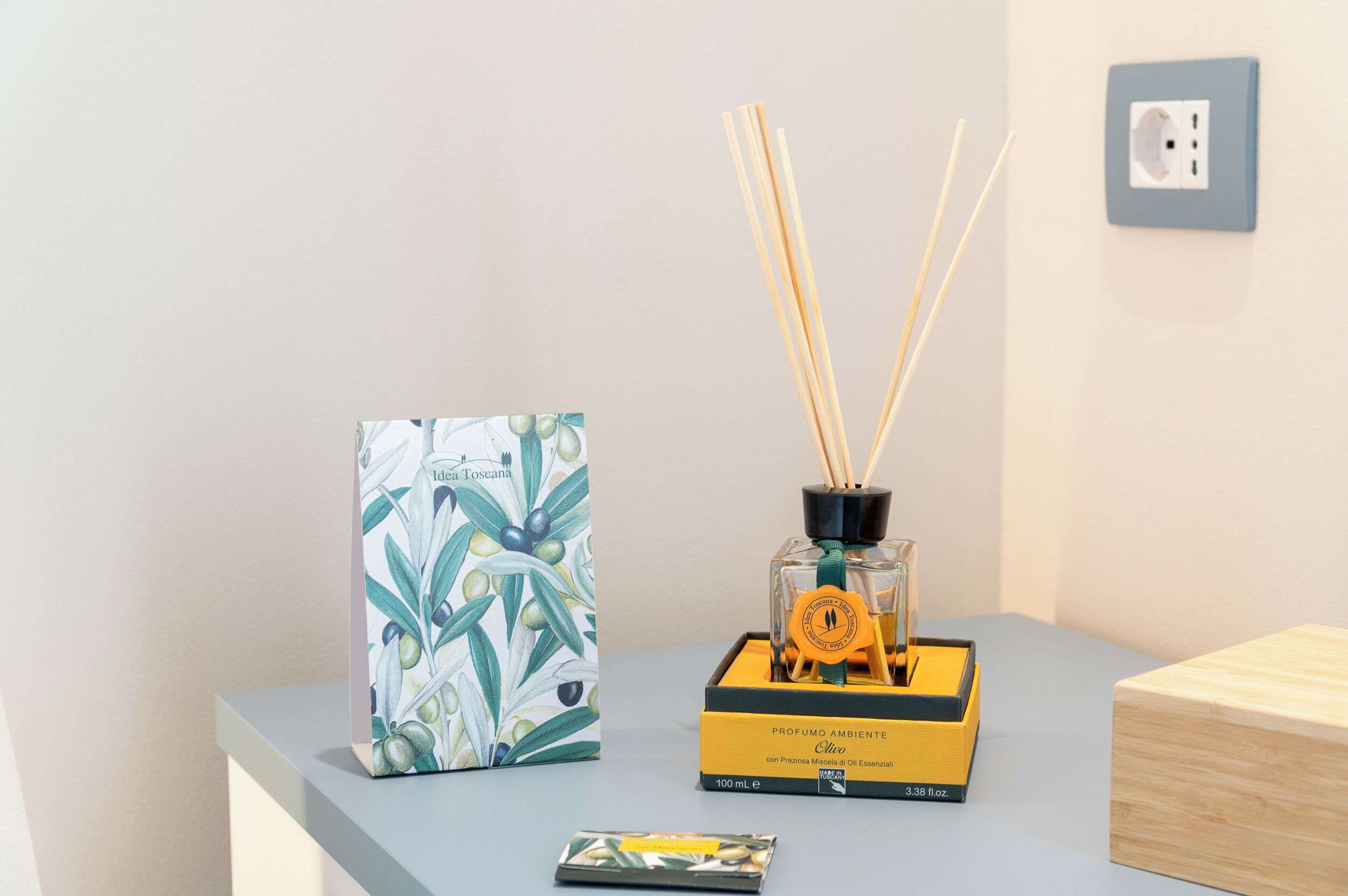 Une petite table sur laquelle se trouvent un diffuseur de parfum à bâtonnets, un tableau encadré et une petite boîte.