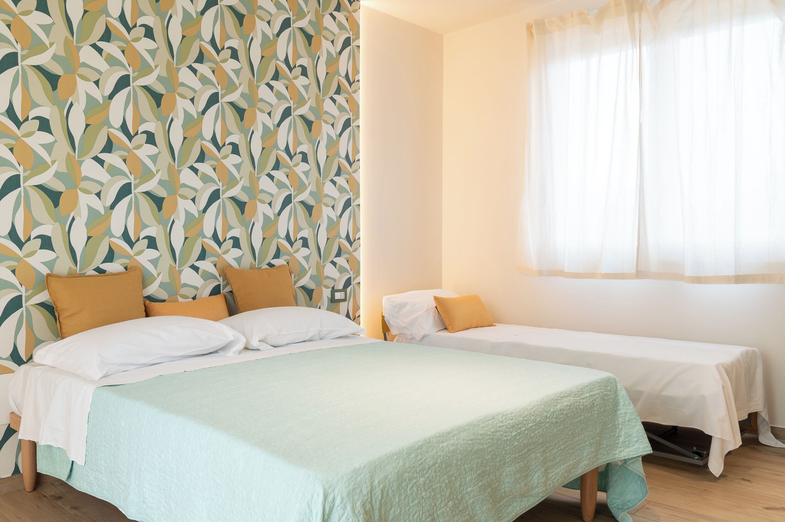 Habitació d'hotel amb dos llits, un mur amb disseny i una finestra amb cortines lleugeres.