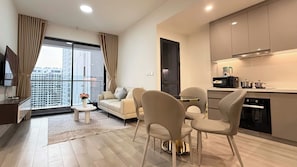 A modern living room with a sofa, chairs, a coffee table, and a kitchen area with appliances. - Tommy Land Vinhomes Grand Park  (Ho Chi Minh City)