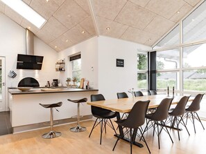 A modern kitchen with a large island, bar stools, and a dining area with a large table and chairs. - 5 Star Holiday Home in Hals (Hals)