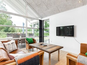 Ein modernes Wohnzimmer mit großem Fernseher, bequemen Sitzmöglichkeiten und Blick ins Grüne.
