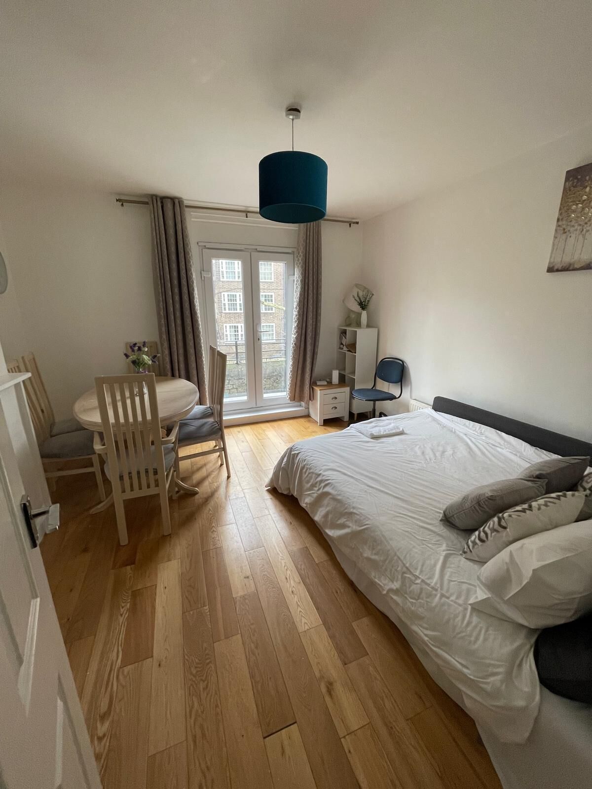 A bedroom with a bed, a desk, and a chair. There is a window with curtains, a door, and a ceiling light.