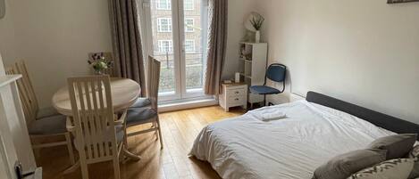 A bedroom with a bed, a desk, and a chair. There is a window with curtains, a door, and a ceiling light.