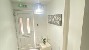 A hallway with a patterned floor, a white door, a radiator, a small plant, a wall-mounted light fixture, and a ceiling-mounted smoke detector. - Luxurious 5 Bedroom Home in Prime London Location (London)