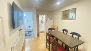 Un coin repas avec une table et des chaises, un téléviseur fixé au mur, un radiateur et, au fond, une cuisine.