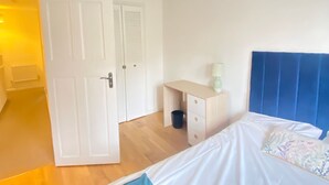 Une chambre à coucher comprenant un lit, un bureau, une armoire et une porte donnant sur une autre pièce.