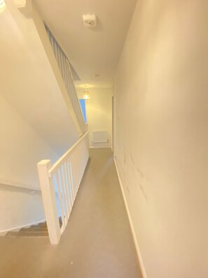 A narrow hallway with a white railing, a radiator, and a light fixture on the ceiling. - Luxurious 5 Bedroom Home in Prime London Location (London)