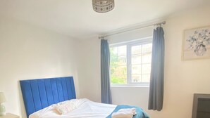 Une chambre à coucher comprenant un lit, une table de chevet, une fenêtre avec des rideaux et un luminaire au plafond.