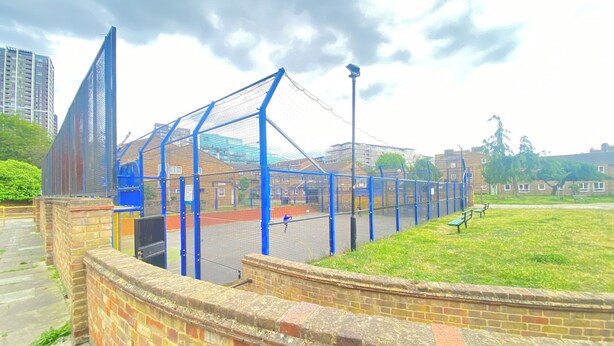 Un complexe sportif doté d’une zone délimitée par une clôture, d’un mur en briques et d’un chemin.