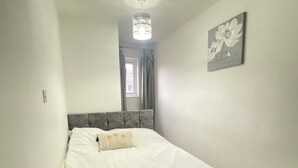 A bedroom with a bed, pillows, a ceiling light, a window with curtains, and a wall art piece. - Luxurious 5 Bedroom Home in Prime London Location (London)