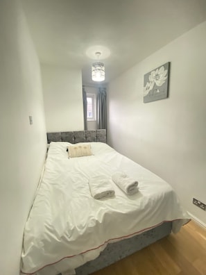 Camera da letto con un letto, cuscini, una lampada a soffitto, una finestra con tende e un quadro appeso al muro.