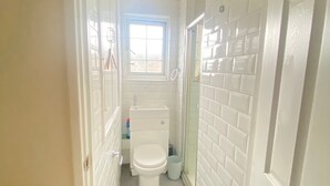 Une petite salle de bain aux murs recouverts de carreaux blancs, avec des toilettes et une fenêtre.