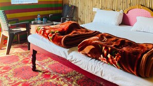 A room with a bed, a chair, a table with a water bottle, a kettle, and a plastic chair. - Prabhu Premi Sevashray (Karchana)