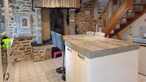 Una cocina con pared de piedra, estufa de leña, escalera de madera y una zona de bar.