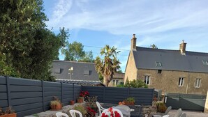 Un patio con mesa y sillas, rodeado de plantas y un muro de piedra.