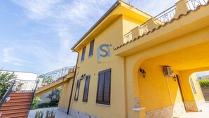 Um edifício amarelo com varanda, escadaria e logotipo lateral.