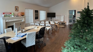 A modern meeting room with a long table, white chairs, a fireplace, a television, and a Christmas tree.