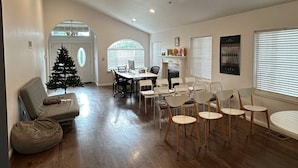 A spacious living room with a wooden floor, a black trampoline, and a patterned rug. There is a Christmas tree and a dining area with chairs and a table.