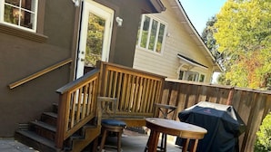 A patio with a wooden deck, a barbecue grill, and a seating area with two chairs and a table.