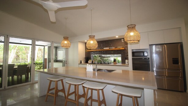 Une cuisine moderne dotée d’un grand îlot central, d’appareils électroménagers en acier inoxydable et de luminaires suspendus en osier.