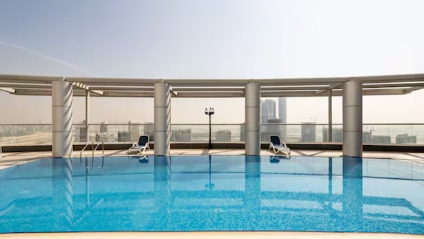 Ein Innenpool mit klarem, blauen Wasser, zwei Liegestühlen und einem Blick auf die Stadt am Horizont.