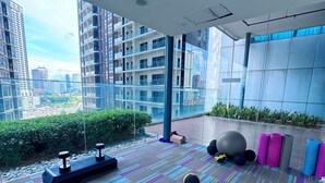 A modern gym with exercise equipment, a patterned floor, and a view of the city through large windows. - MERCU SUMMER SUITES MINUTES TO KLCC BY JK PRIVY HOMES (Kuala Lumpur)