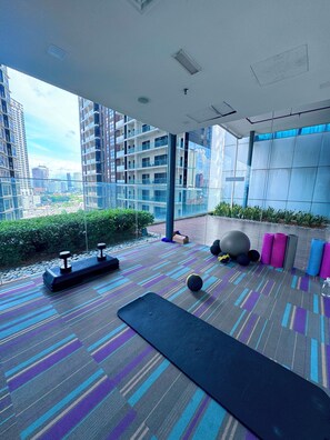 Un gimnasio moderno con equipamiento de ejercicio, piso estampado y vistas de la ciudad a través de amplias ventanas.