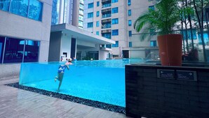 A swimming pool area with a person swimming, surrounded by high-rise buildings and a potted plant. - MERCU SUMMER SUITES MINUTES TO KLCC BY JK PRIVY HOMES (Kuala Lumpur)