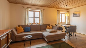 A cozy living room with a sectional sofa, a small round table, and a dining area with chairs. - Panoramic view apartment with infrared sauna in the middle of the Bavarian Sonnenwald (Grattersdorf)