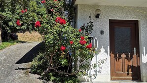 A building with a wooden balcony, a door with a number plate, and a garden with red flowers. - Panoramic view apartment with infrared sauna in the middle of the Bavarian Sonnenwald (Grattersdorf)