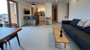 Een moderne woonkamer met een bank, een houten salontafel en een eethoek met een tafel en stoelen.
