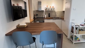 Een moderne keuken met een houten eiland, twee blauwe stoelen, een ingebouwde televisie en een witte boekenkast.