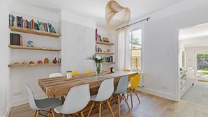 Ein Essbereich mit einem Holztisch, weißen und gelben Stühlen sowie Bücherregalen an der Wand.